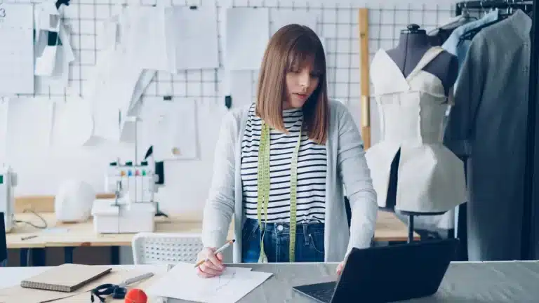 Designer working intensely at a workspace surrounded by fabric samples and creative materials in a modern studio setting