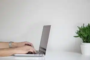 Hands holding a passport and visa forms on a desk with a laptop and coffee