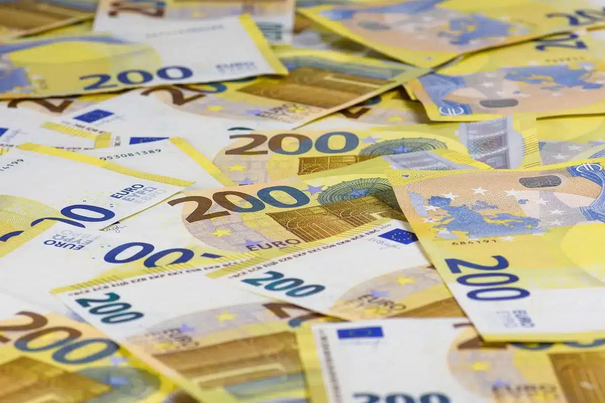 Piggy bank overflowing with coins and bills next to financial charts showing declining trends