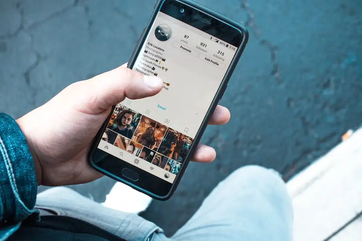 Hands holding a generic contactless card and smartphone showing a payments app on a café table